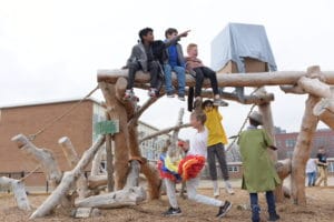 A group of 5 children sit and play on large wood elements of obstacle course that they have built at summer camp at Urban Prairie Waldorf School.