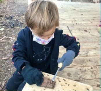 Young Child uses chisel to work on wood working project while at camp.
